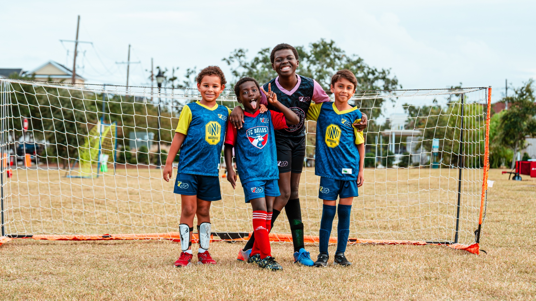 Four young players posing in front of a soccer goal